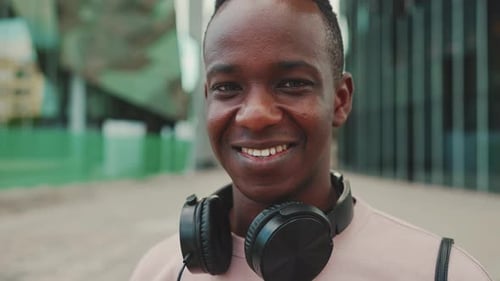 Clouse up, smiling young student stands outside of university in headphones