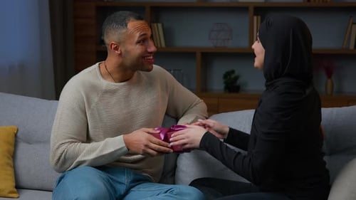 Happy Husband Receive Gift Box From Loving Wife Arabian Muslim Woman in Hijab Hugging African