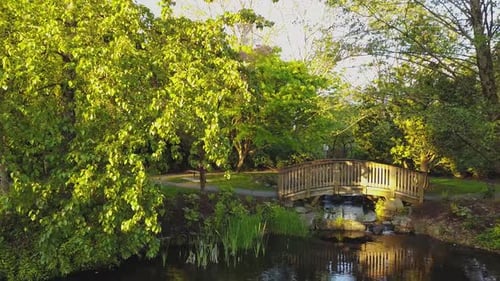 See in einem Park mit einer Holzbrücke über einen fließenden Fluss