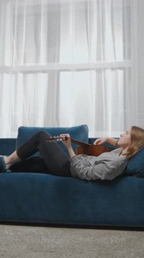 Woman Lying on Couch Plays Guitar Indoors