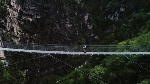Man Crosses Suspension Bridge Over Deep Forest Gorge in Austrian Mountains, Summer