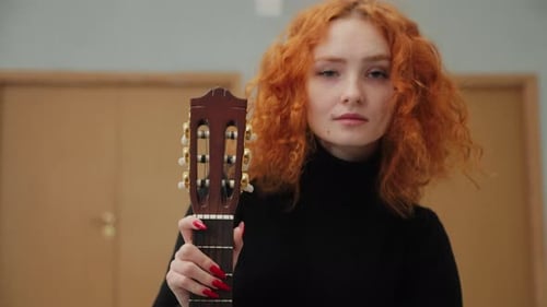 Young Woman Holds Guitar in Indoor Setting