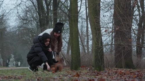 Mother and son hand-feeding a playful wild squirrel in a winter city park