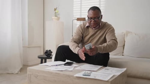 Man Counting Money at Home with Bills Nearby