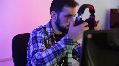 Young Adult Putting on Gaming Headphones at Computer