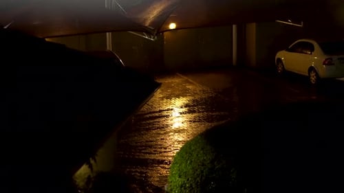 Rainy night shot of eerie parking lot with warm light lighting the car port.