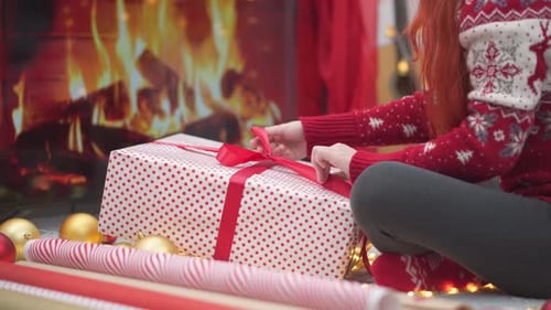Woman Wrapping Christmas Gift by Cozy Fireplace
