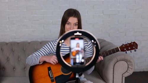 Woman Plays Guitar and Sings in Front of Phone