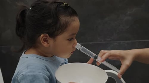 mother making nasal wash for toddler girl with syringe and saline. cleaning nose