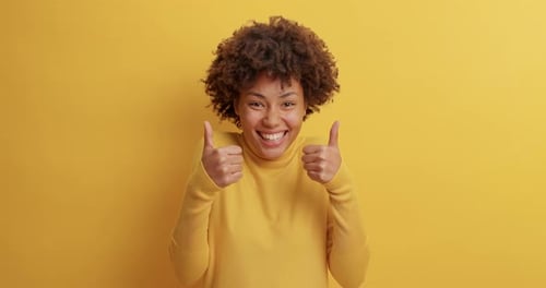 Enthusiastic Young Woman Giving Thumbs Up on Yellow Backdrop
