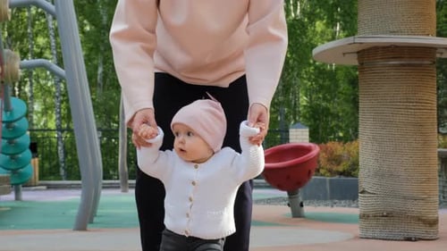 Young Mother Teaching Baby to Walk on Playground