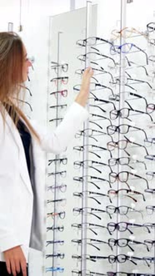 Customer in eyeglasses store. View of woman choosing eyeglasses from rack