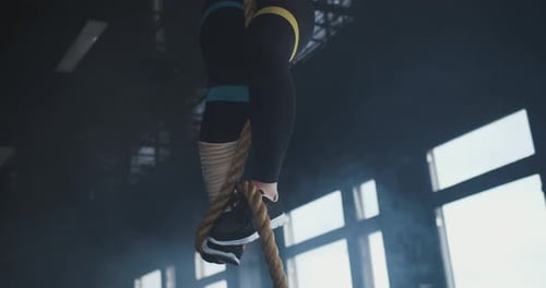 Young Happy Strong Athletic Blonde Woman Climbs Rope Jumps Down Breathing Heavy at Cross Fit Workout