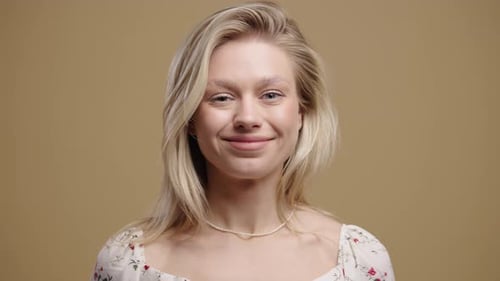 Smiling blonde woman winks playfully on neutral background