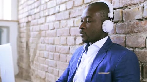 Man with Headphones Working on Laptop by Brick Wall