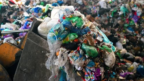 An excavator carries waste into a large heap of garbage at waste sorting plant. Slow motion
