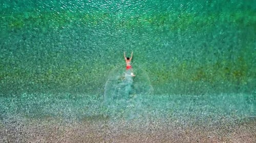 Aerial View of a Man in Red Shorts Swims in the Crystal Clear Sea Water
