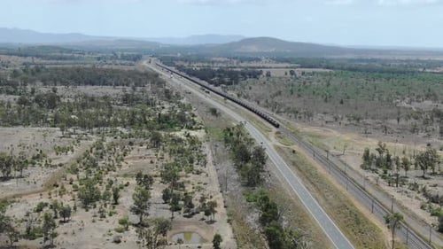 Train running on railway parallel to road at Bajool in Queensland, Australia. Aerial drone panoramic