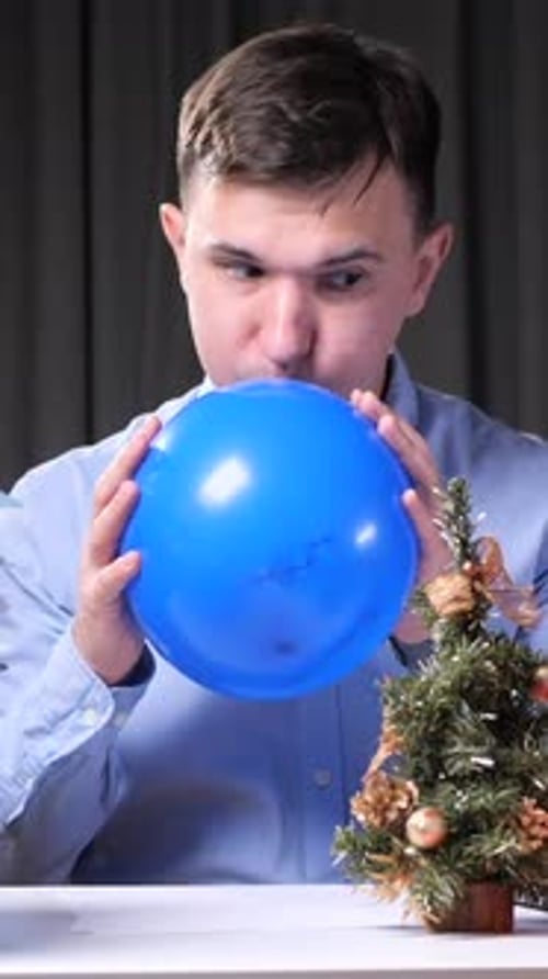Young Adult Inflating Blue Balloon by Christmas Tree