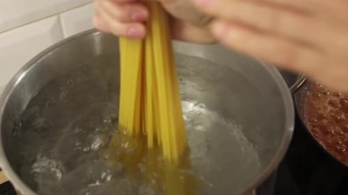 Spaghetti pasta being artistically dropped into boiling water inside metal pot during cooking.