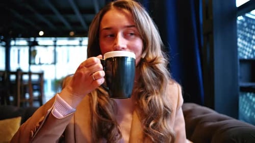 Woman drinking coffee cappuccino from a black and white cup at a restaurant