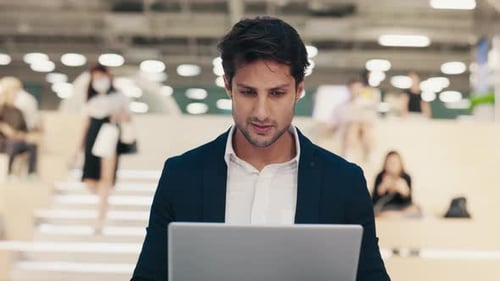 Professional Man Working on Laptop in Modern Office Environment With Colleagues Nearby During