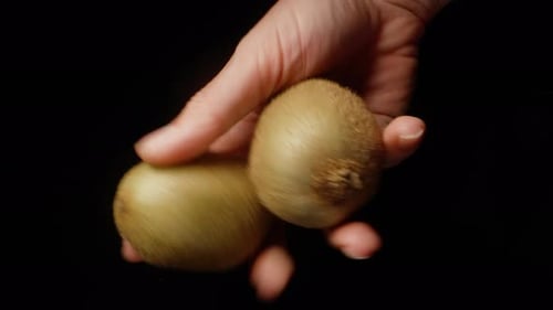 The young woman turns two kiwis in her hand on a black background.