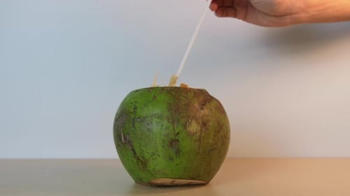 Person inserting a straw into a delicious green coconut in slow motion. Exotic fruits of tropical re