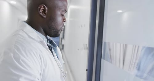 Stressed african american male doctor leaning on door in hospital in slow motion