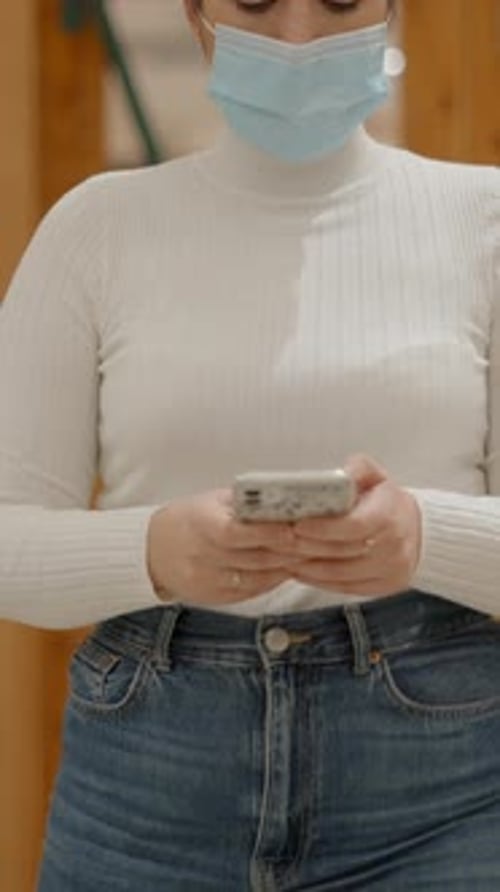 Safety in the Office During COVID19 Pandemic Woman in Face Mask Texting on Phone While Walking