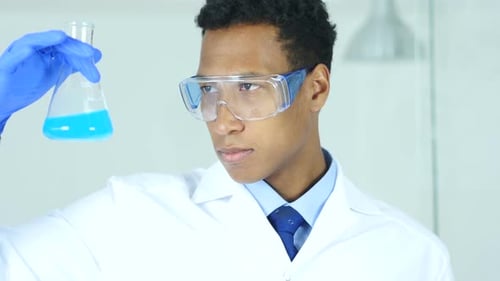 Scientist in Lab Examines Blue Liquid in Flask