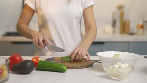 Woman Slicing Cucumber for Salad in Kitchen