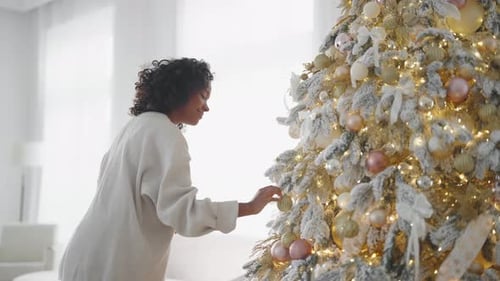 Woman Decorates Christmas Tree With Gold Ornaments at Home