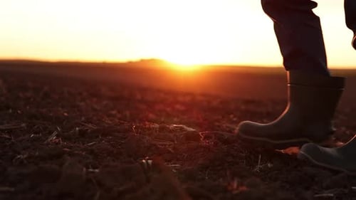 Agriculture. Cropped shot of back view businessman farmer in rubber boots walks along plowed field