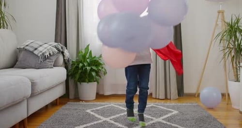 Child in Superhero Costume with Red Cape and Mask Playing with Balloons in Home