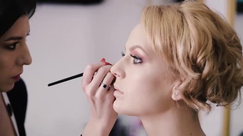 Der dunkelhaarige Visagist schminkt die Augen auf das schöne blonde Model