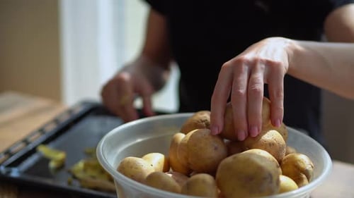 Hand Of A Woman Picking Up Raw Potatoes From A Plastic Bowl To Peel Using A Peeler. - Rack Focus