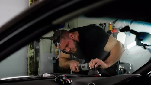 Man Buffing Car Dashboard with Power Tool Indoors