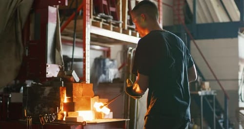 Professional metalsmith forging red hot metal on anvil in dark blacksmith workshop