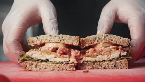 Hands separate chicken sandwich on cutting board