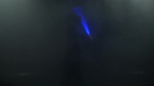 Young Man in Jedi Cosplay Costume with Lightsaber Battle on Black Background in Smoke and Rain Slow