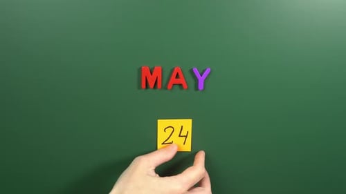 Hand sticking a sticker 24 May calendar day on school board. 24 date of May. Twenty fourth day