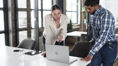 Young Caucasian woman and Asian man review business content on a laptop in an office