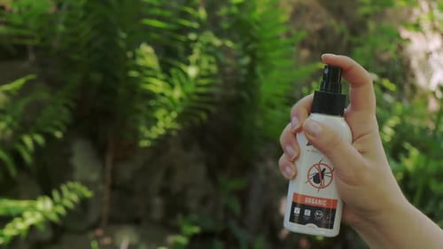 Woman hand spraying anti-tick spray on a green natural background 100p slow motion