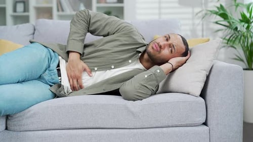 Young adult man lying on the couch feeling sudden strong abdominal stomach ache, gastritis problem.