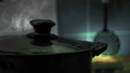 Man Removes Lid From Pot with Boiling Liquid on Stove and Steam Comes Out of It