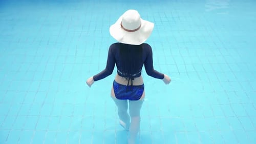 Woman tourist in bikini swimsuit with sun hat relaxing tropical lux hotel, walks into swimming pool