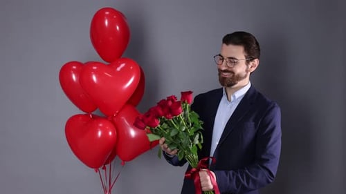 St. Valentine's Day. Man with bouquet of roses and heart shaped balloons on grey background