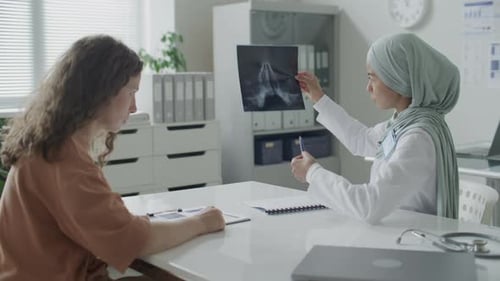 Female Doctor in Hijab Discussing X-Ray with Patient in Medical Office
