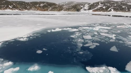Drone Over Ice And Snow In Sea Towards Rocky Coastline Of Greenland